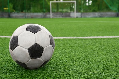 Dirty soccer ball on green football field, space for text