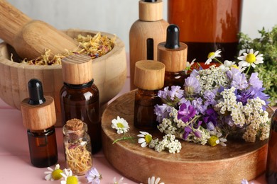 Photo of Aromatherapy. Different essential oils, mortar, pestle and flowers on pink wooden table