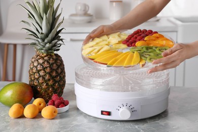 Photo of Woman putting tray with cut fruits into dehydrator machine at grey marble table in kitchen, closeup