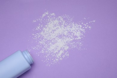 Bottle and scattered dusting powder on violet background, top view. Baby cosmetic product