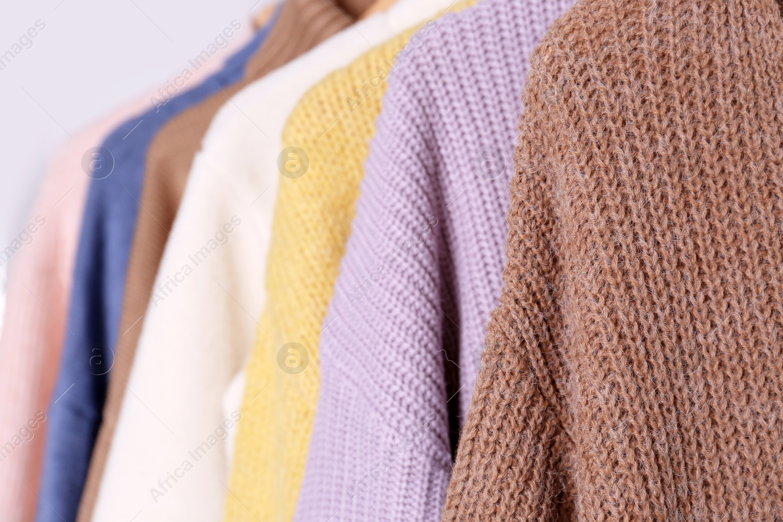 Photo of Warm sweaters hanging on rack, closeup view