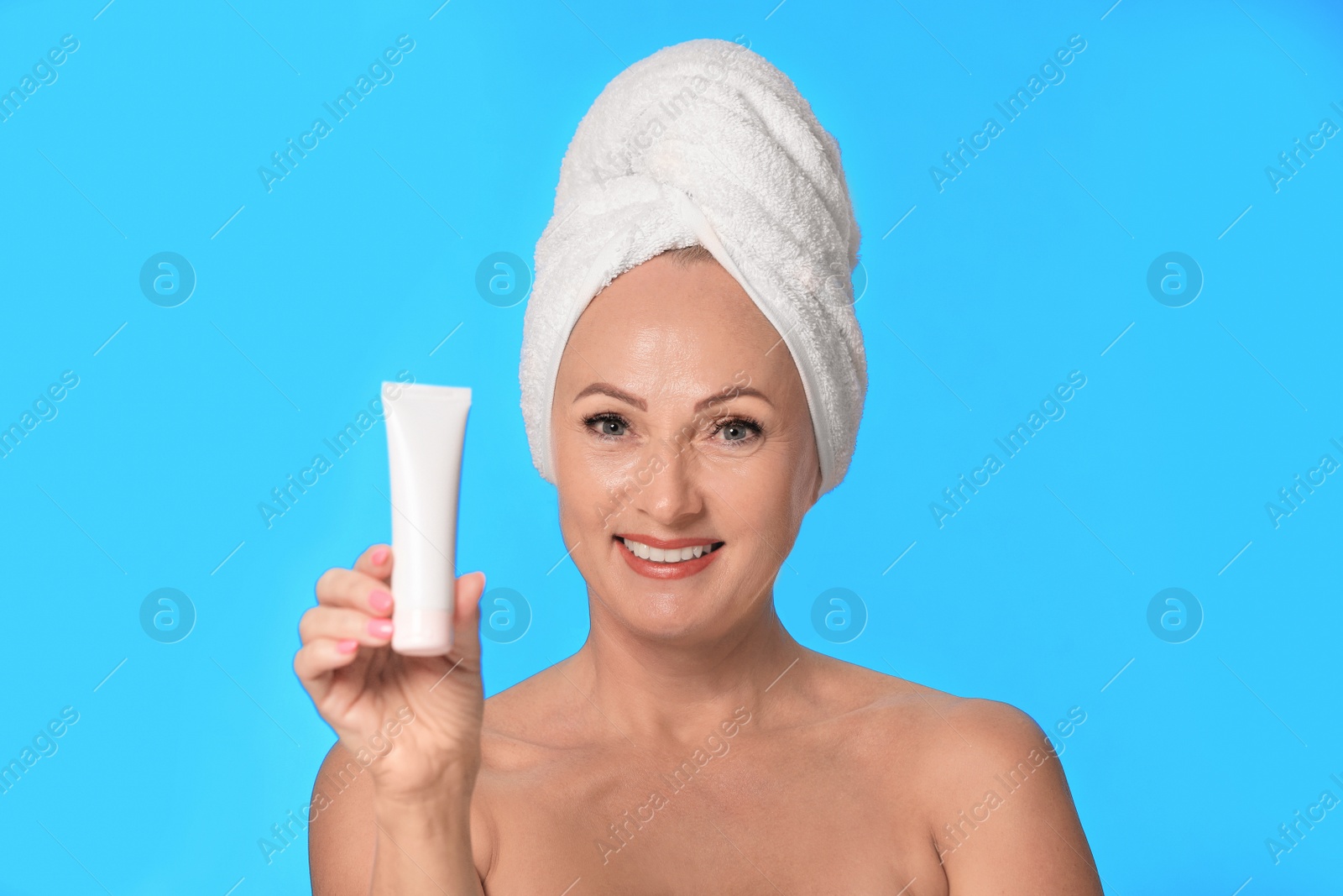 Photo of Portrait of beautiful mature woman with perfect skin holding tube of cream on light blue background