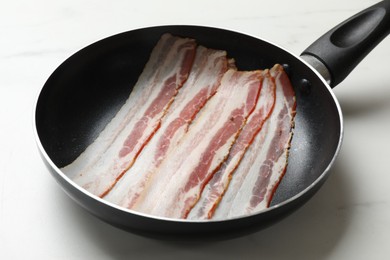 Slices of raw bacon in frying pan on light table, closeup