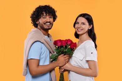 International dating. Happy couple with bouquet of roses on yellow background