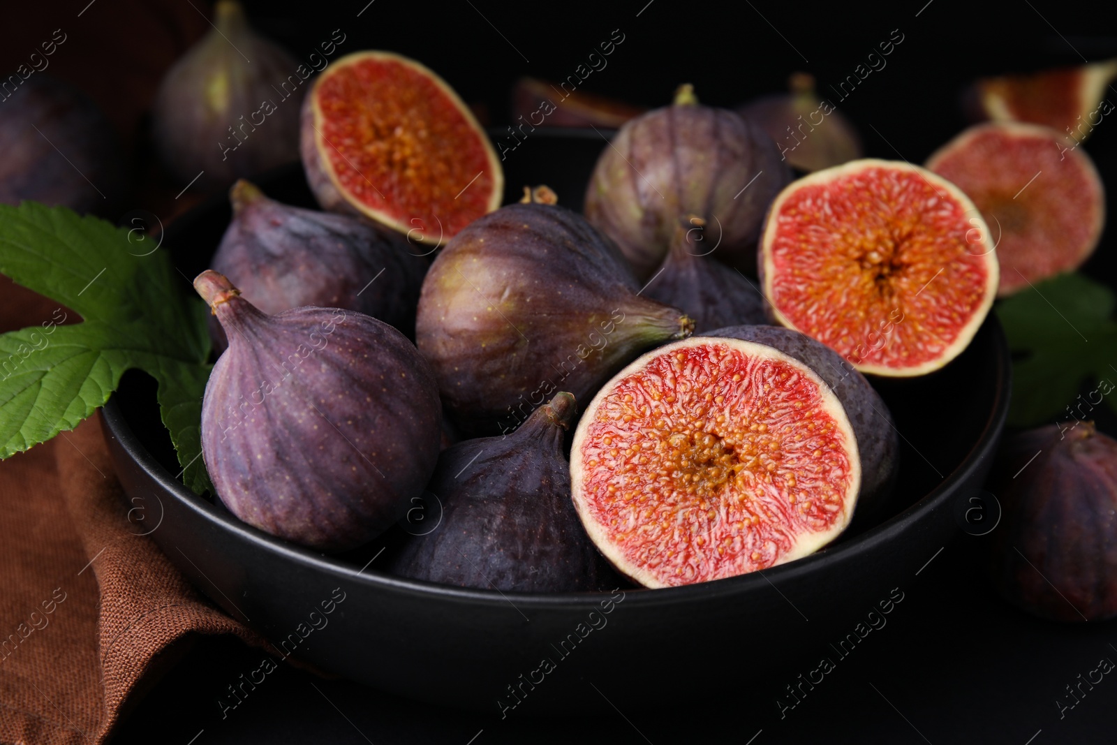 Photo of Bowl with fresh ripe purple figs on black table