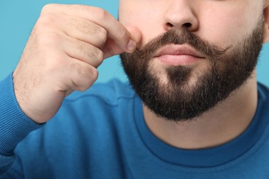 Photo of Man touching mustache on light blue background, closeup