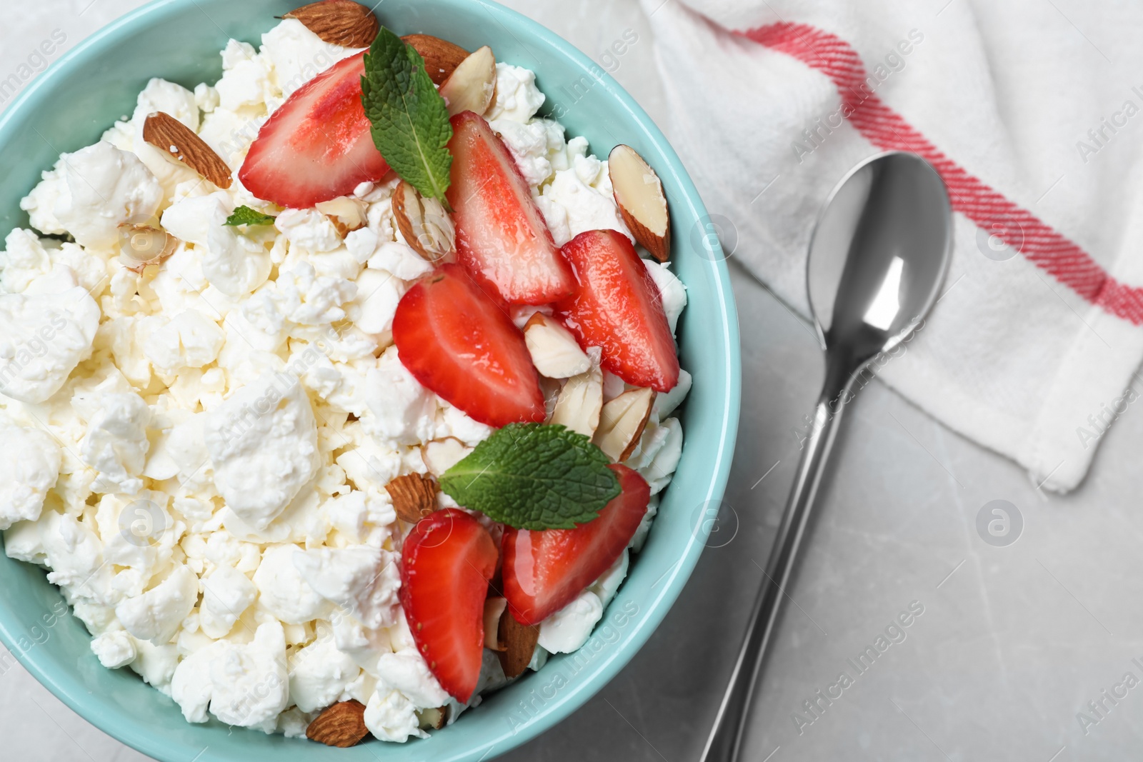 Photo of Fresh cottage cheese with strawberry and almond in bowl on light marble table, flat lay