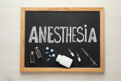 Photo of Blackboard with word Anesthesia, syringe and drugs on white wooden table, top view