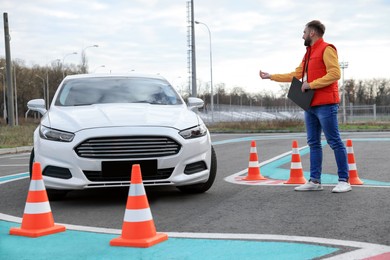 Photo of Instructor near car with his student during exam at driving school test track