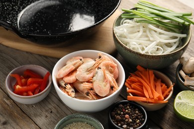 Different products and black wok on wooden table, closeup