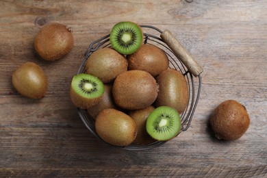 Photo of Metal basket with cut and whole fresh kiwis on wooden table, flat lay
