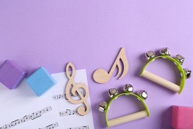 Photo of Tools for creating baby songs. Flat lay composition with wooden notes and tambourines for kids on violet background