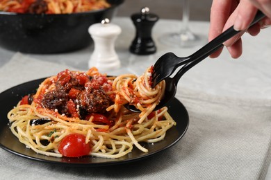 Woman eating delicious pasta with meatballs and tomato sauce at table, closeup