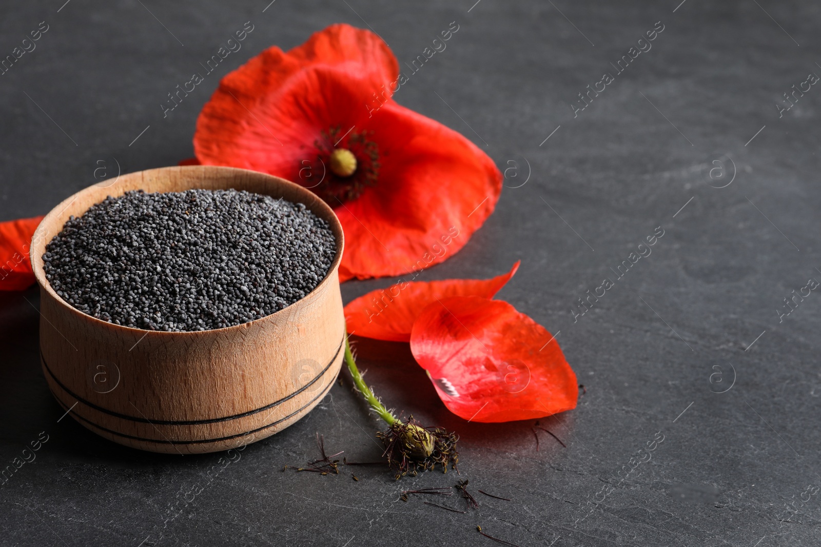 Photo of Wooden bowl of poppy seeds and flower on grey table, space for text