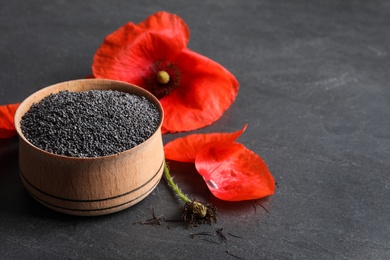 Wooden bowl of poppy seeds and flower on grey table, space for text