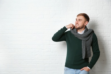 Photo of Handsome young man in warm sweater with scarf near white brick wall. Space for text