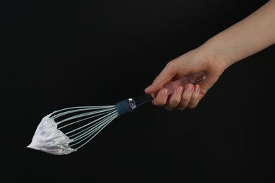 Woman holding whisk with whipped cream on black background, closeup