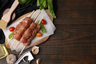Photo of Skewers with cut raw marinated meat on wooden table, flat lay. Space for text