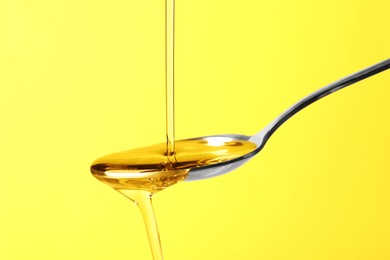 Photo of Pouring cooking oil into spoon on yellow background, closeup