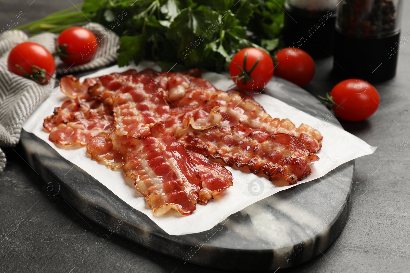 Photo of Fried bacon slices, tomatoes and parsley on dark table, closeup