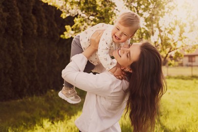 Happy mother playing with her cute baby in park on sunny day