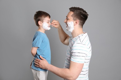 Photo of Dad pretending to shave his little son on color background