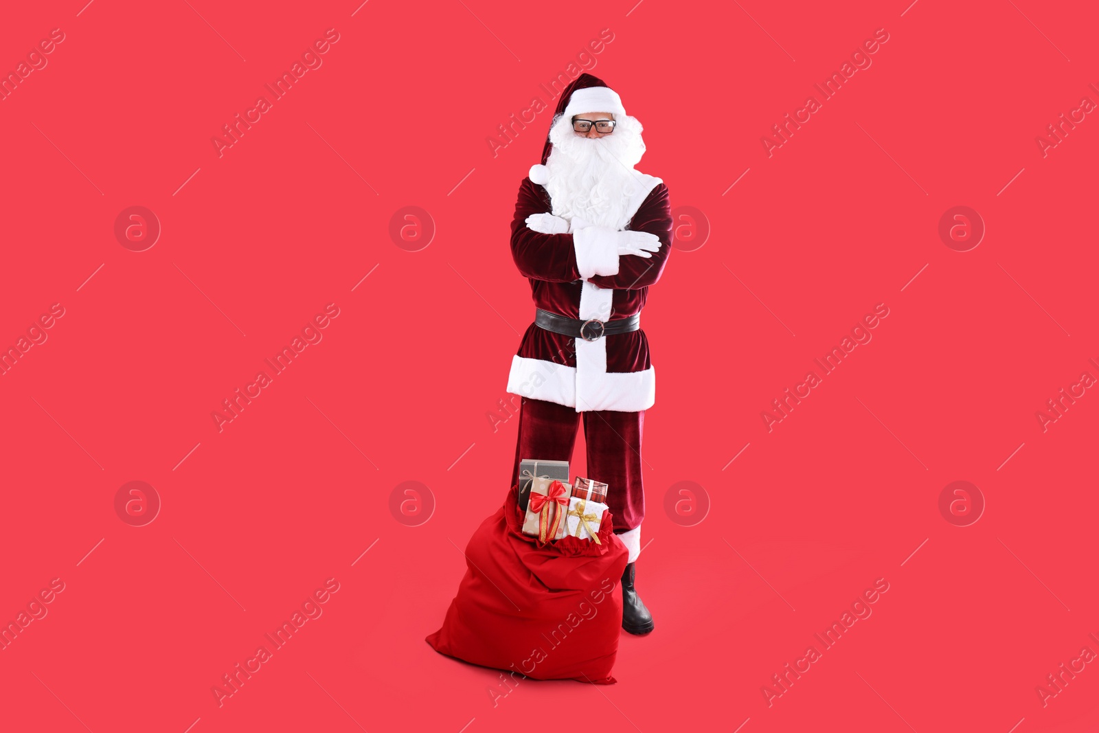 Photo of Santa Claus near sack with gift boxes on red background