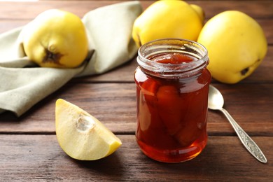 Photo of Tasty homemade quince jam in jar and fruits on wooden table