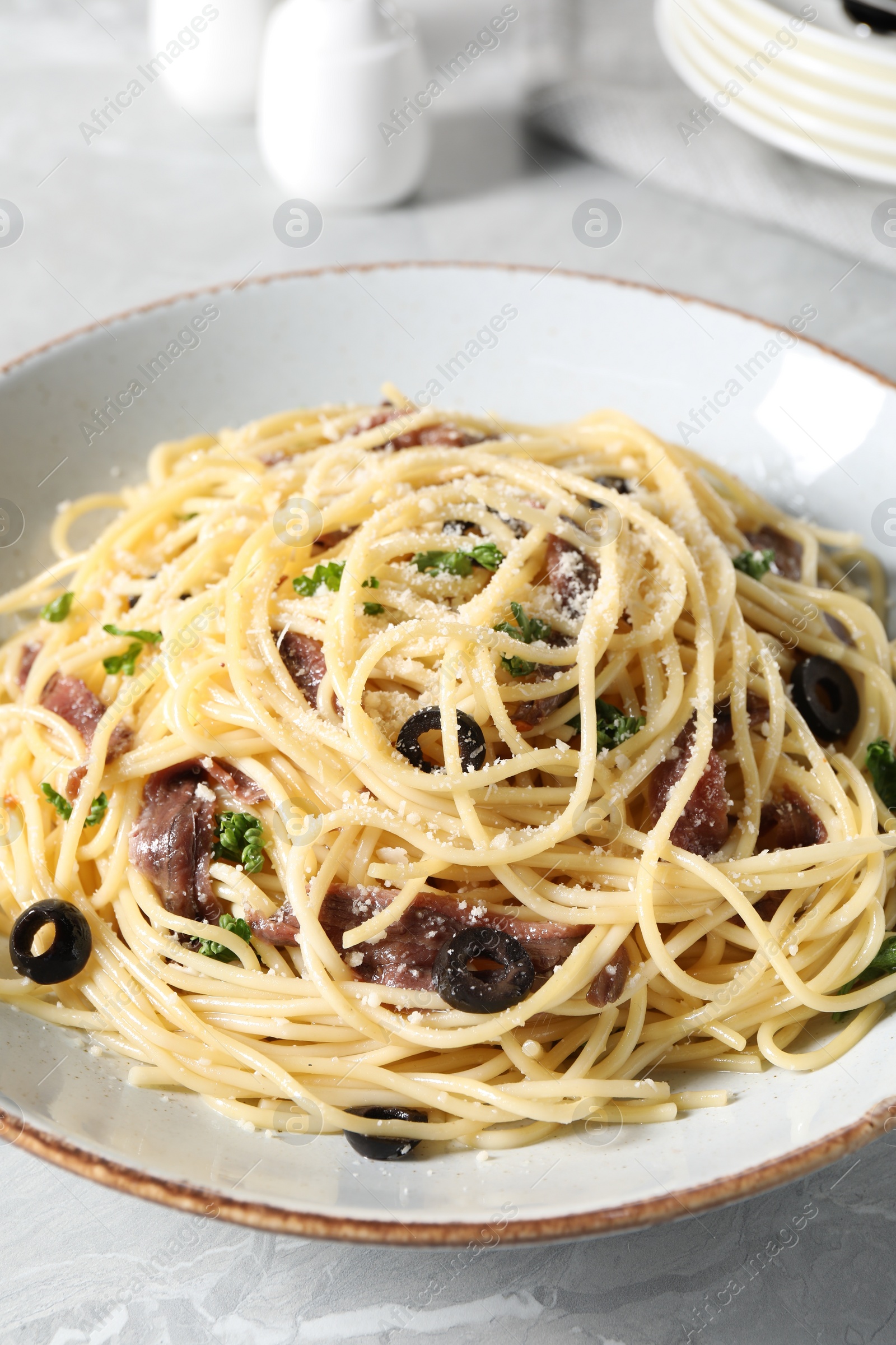 Photo of Delicious pasta with anchovies, olives and parmesan cheese served on grey marble table, closeup