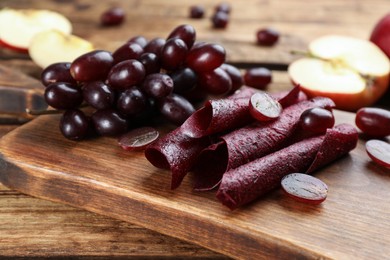 Photo of Delicious fruit leather rolls and grapes on wooden table, closeup