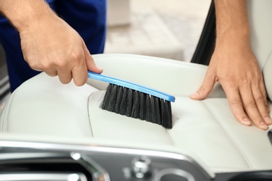 Photo of Man cleaning seat with brush, closeup. Car wash