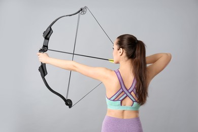 Young woman practicing archery on light grey background, back view