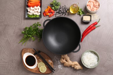 Photo of Wok, chopsticks and different products on grey textured table, flat lay