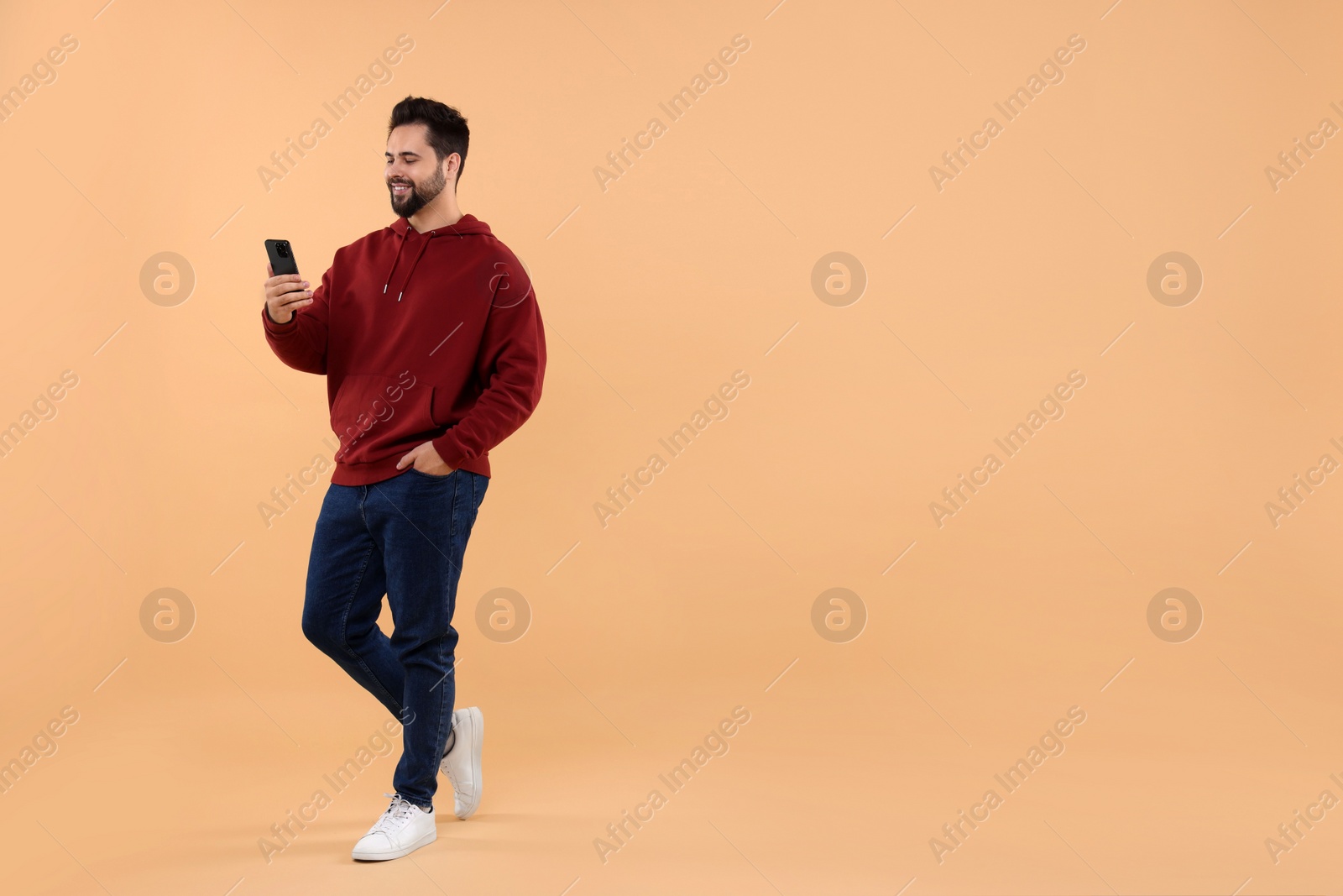 Photo of Happy young man using smartphone on beige background, space for text