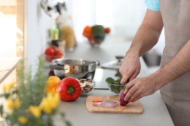 Young man cutting vegetables for soup in kitchen, closeup