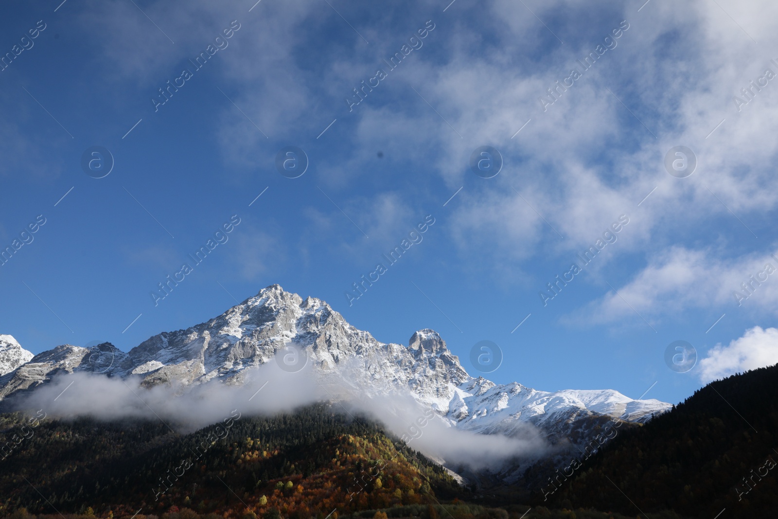 Photo of Picturesque landscape of high mountains covered with thick mist under blue sky on autumn day