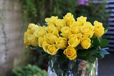 Photo of Beautiful bouquet of yellow roses in glass vase outdoors