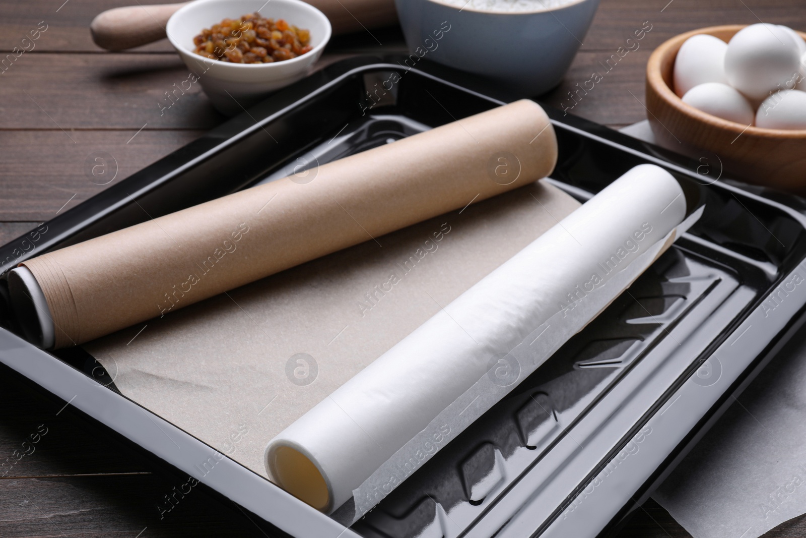 Photo of Rolls of parchment paper in baking pan and different ingredients on wooden table