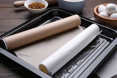 Rolls of parchment paper in baking pan and different ingredients on wooden table