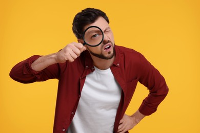 Photo of Confused man looking through magnifier glass on yellow background