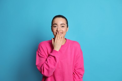 Beautiful young woman laughing on light blue background. Funny joke