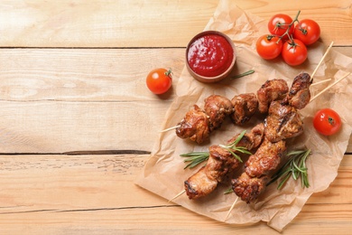 Delicious barbecued meat served with sauce and garnish on wooden background, top view. Space for text