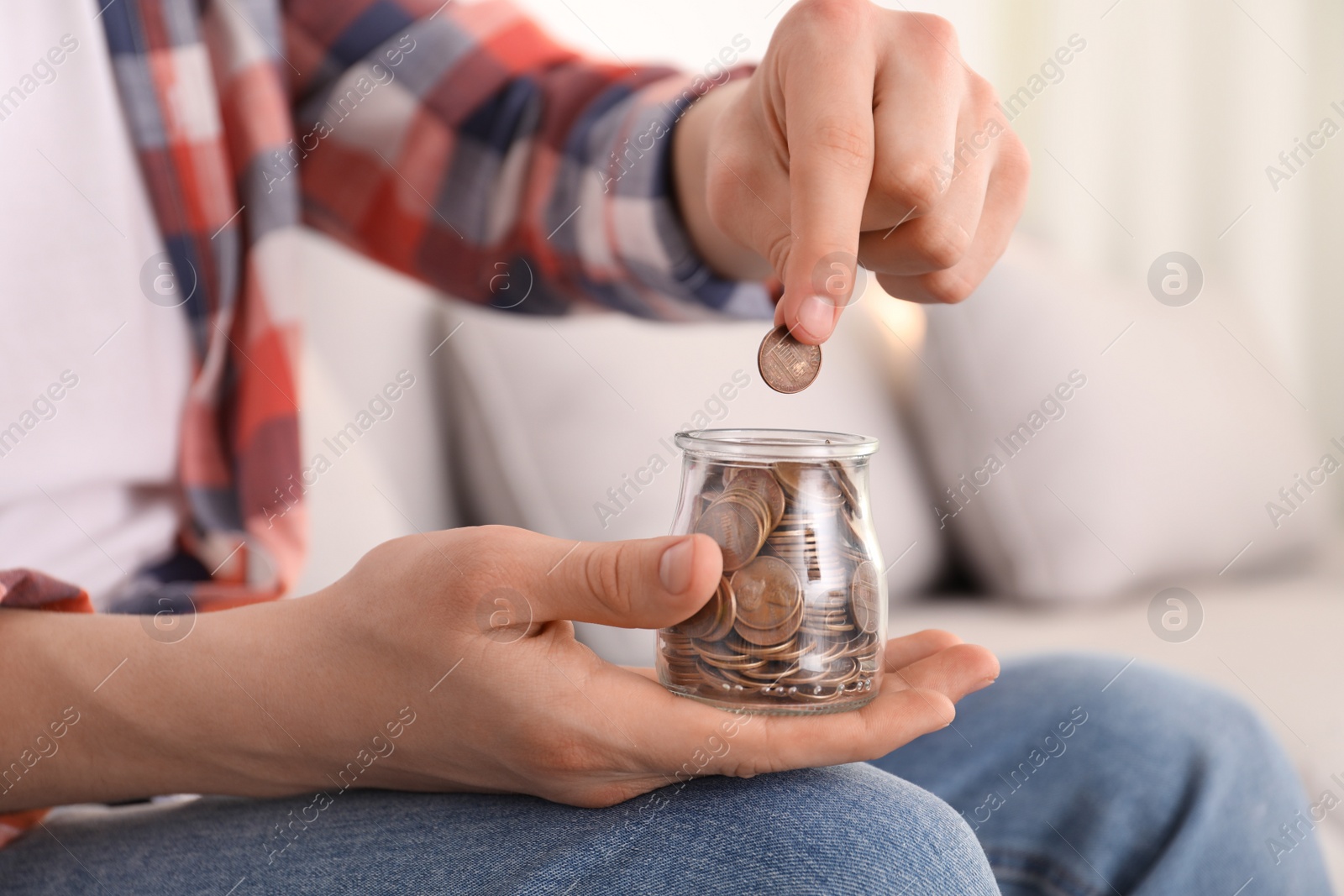 Photo of Man putting coin into glass jar at home, closeup