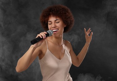 Photo of Curly young woman with microphone singing in smoke on black background