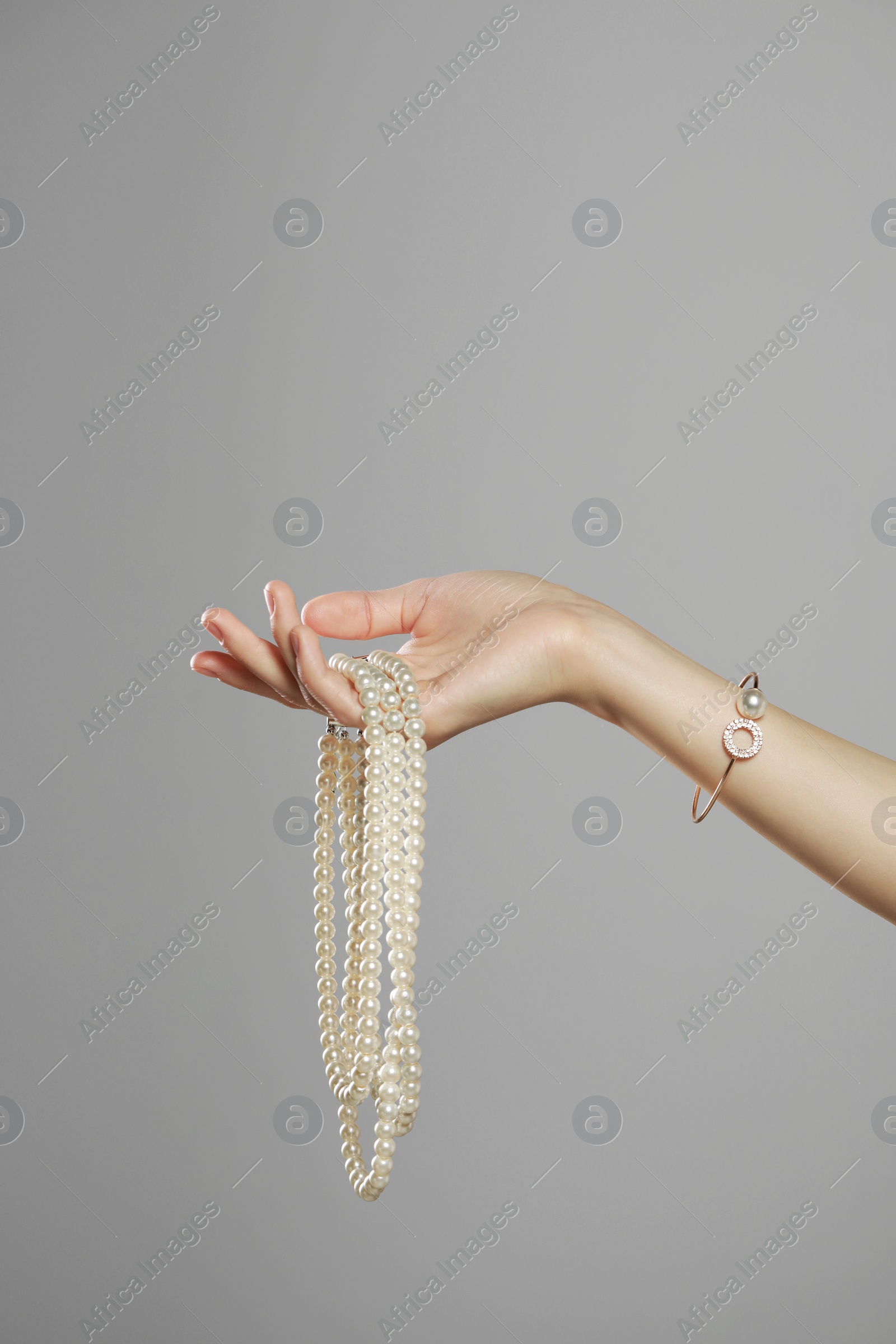 Photo of Young woman with elegant pearl jewelry on grey background, closeup