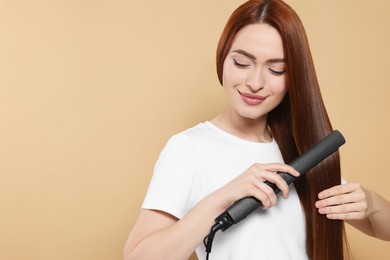 Photo of Beautiful woman using hair iron on beige background, space for text