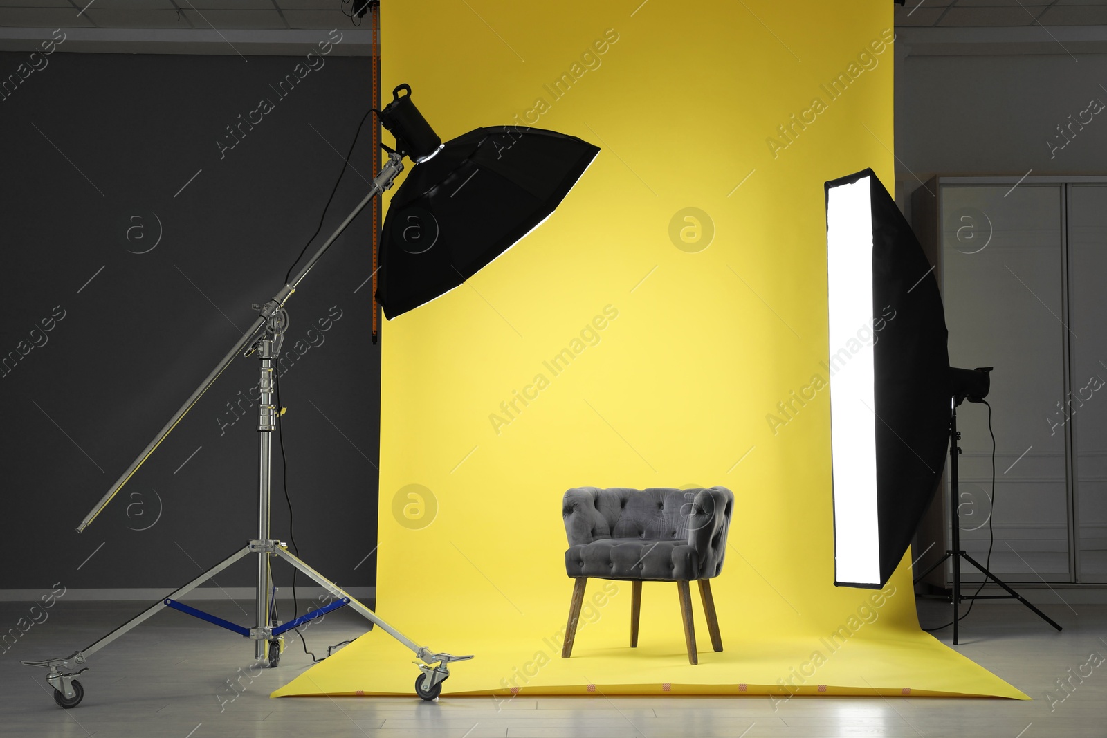 Photo of Yellow photo background, armchair and professional lighting equipment in modern studio