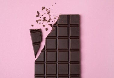 Photo of Broken dark chocolate bar on pink background, flat lay