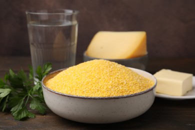 Raw cornmeal in bowl and products on wooden table, closeup