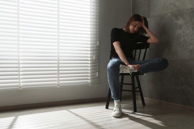 Photo of Sad young woman sitting on chair at home, space for text